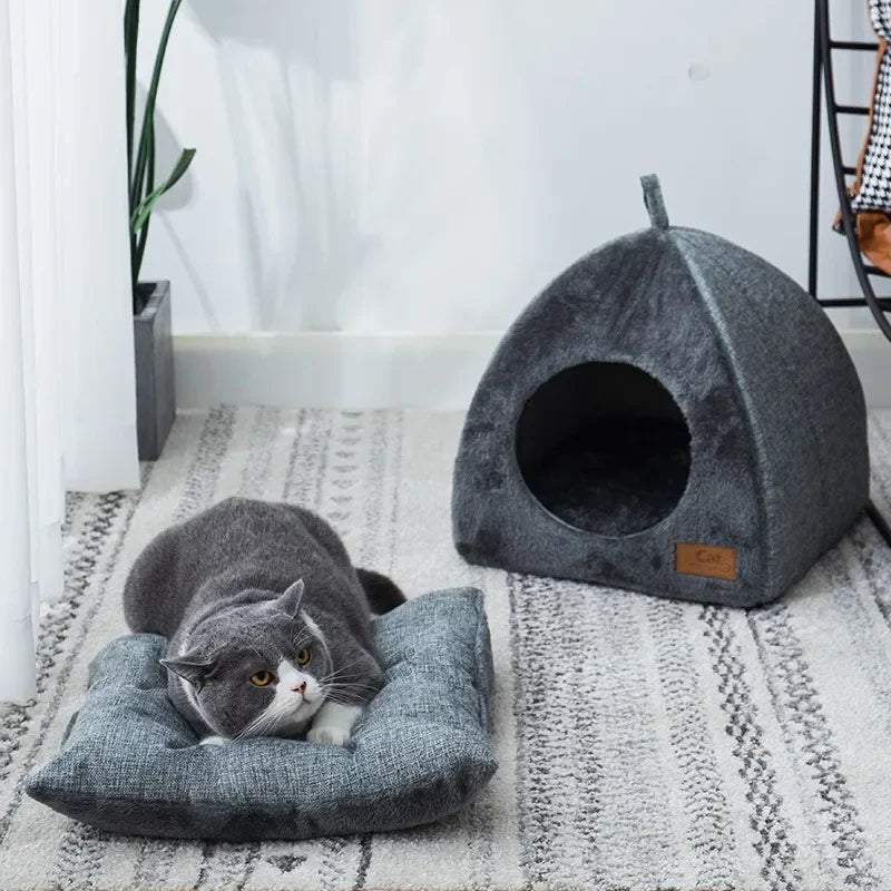 Gray cat lying on a matching cushion next to a gray pet bed in a home setting.