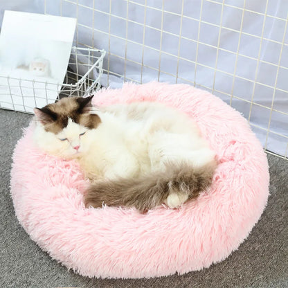 Cat lying on a fluffy pink pet bed with a white basket in the background.